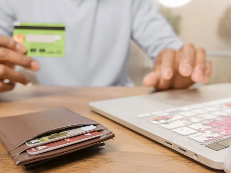 Hands holding a payment card beside a laptop.